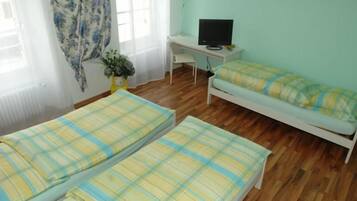 A room with two beds, a desk with a computer, and a window with curtains.