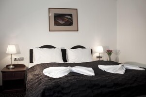 Una habitación de hotel con una cama, dos lámparas de noche, un cuadro en la pared y un florero con flores en la mesita de noche.
