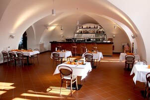 Un restaurante con varias mesas y sillas, una zona de bar con estantes llenos de botellas y un suelo de baldosas.