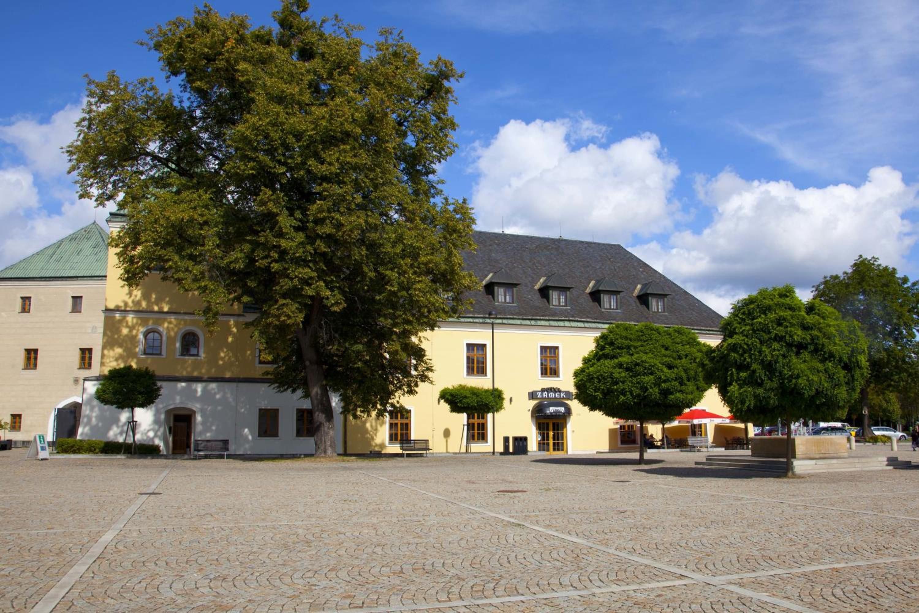 A courtyard with a building featuring a green roof and a yellow facade.