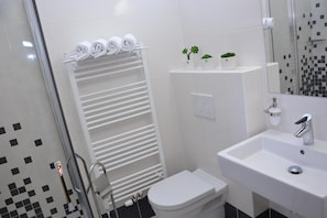 A bathroom with a white toilet, a sink with a modern faucet, a towel rack with rolled towels, and a shower area with a glass door.