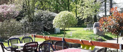 An outdoor seating area with tables and chairs, surrounded by trees and a stone wall.