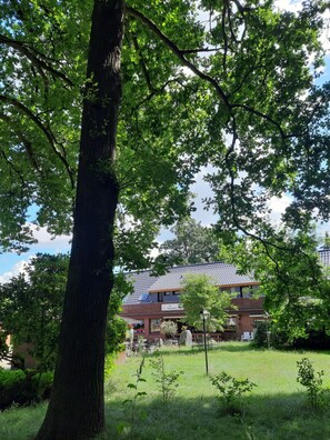 A building with a sloped roof, surrounded by trees and grass. - Pension Im Rehwinkel (Soltau)