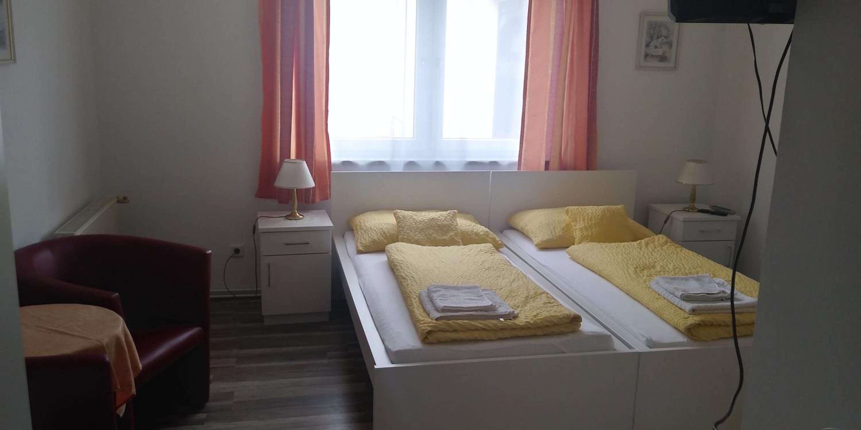 A small, simple room with a bed, a chair, a desk, and a window with curtains.