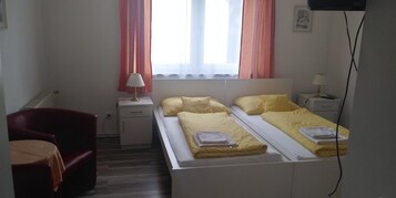Una habitación pequeña y sencilla con una cama, una silla, un escritorio y una ventana con cortinas.