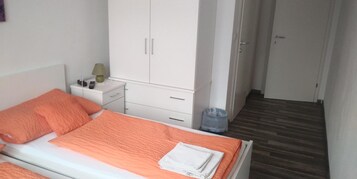 Un dormitorio con cama, mesita de noche, armario y cesto de basura.