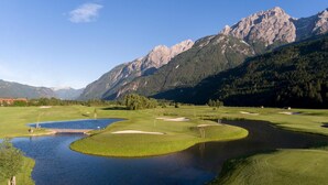 Ein Golfplatz mit mehreren Teichen, blauem Himmel und Bergen im Hintergrund.