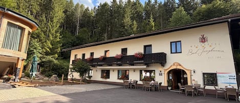 Un hotel con balcón, mobiliario exterior y un paisaje boscoso de fondo.