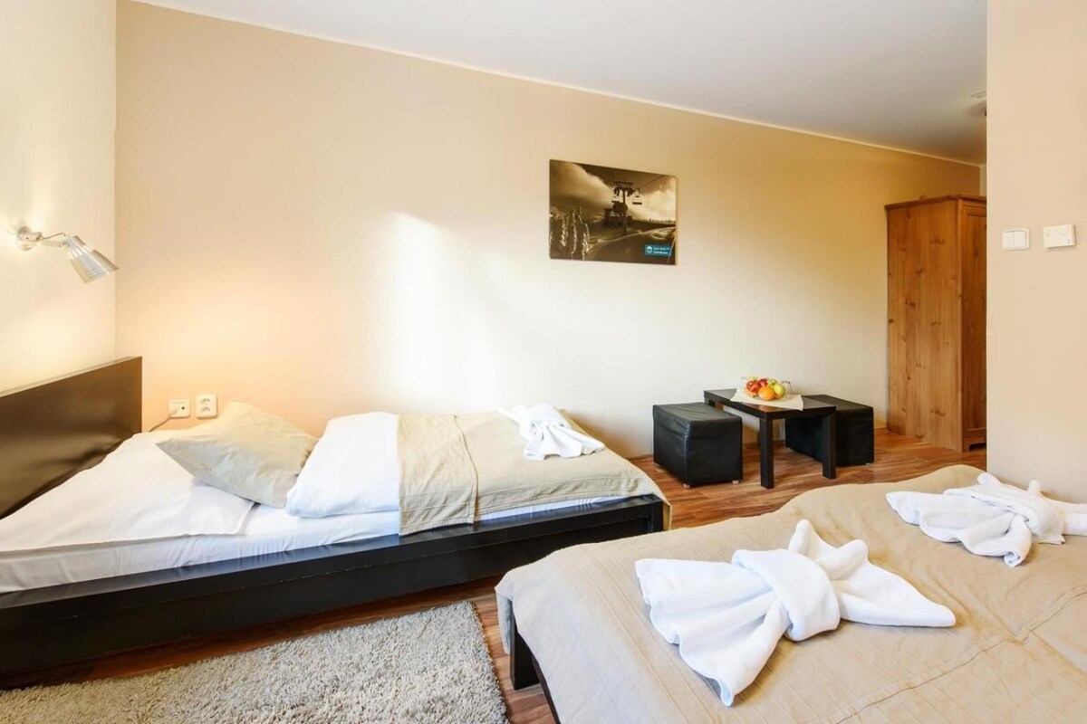 Quarto de hotel com duas camas, uma escrivaninha, uma cadeira, guarda-roupa de madeira e um quadro na parede.