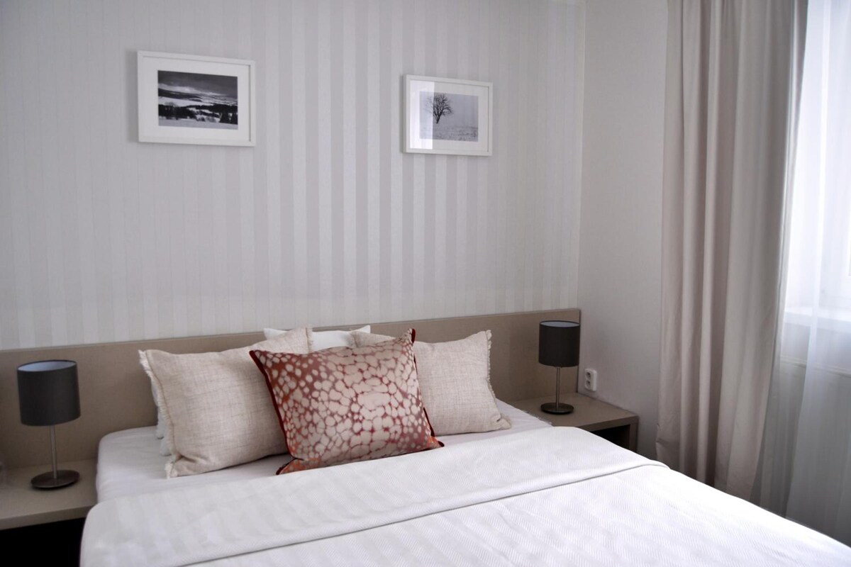 Quarto de hotel com uma cama, duas mesas de cabeceira, duas luminárias e duas quadros pendurados na parede.
