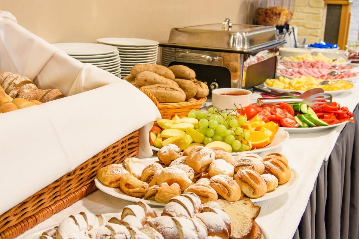Buffet com diversos alimentos, incluindo pães, doces, frutas e legumes.