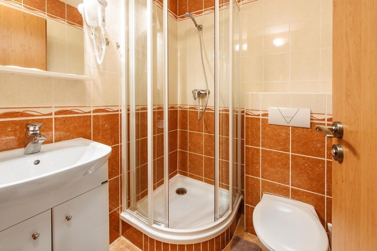 Casa de banho com cabine de hidromassagem em vidro, lavatório e sanita.
