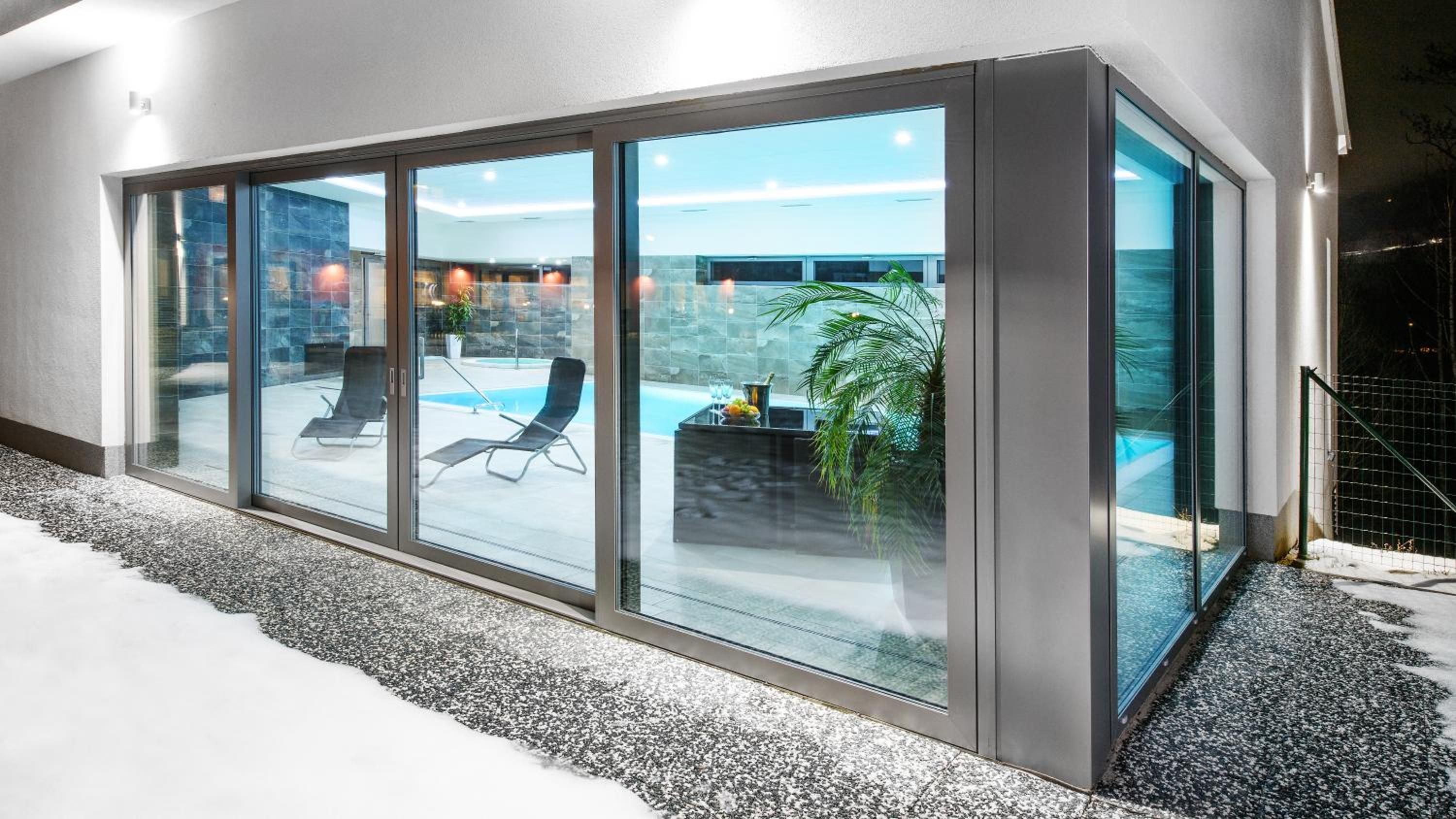 Un edificio moderno con amplios puertas correderas de vidrio que dan a una zona de piscina con tumbonas.