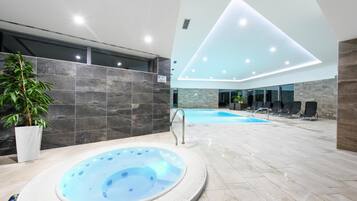 A modern indoor swimming pool area with a hot tub, lounge chairs, and a potted plant.