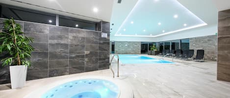 A modern indoor swimming pool area with a hot tub, lounge chairs, and a potted plant.