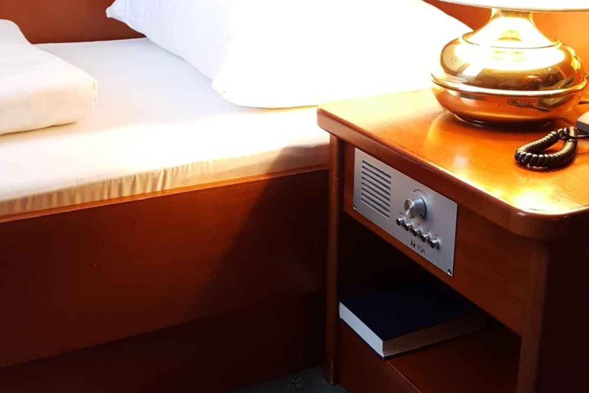 A hotel room with a bed, a bedside table with a lamp, and a drawer.