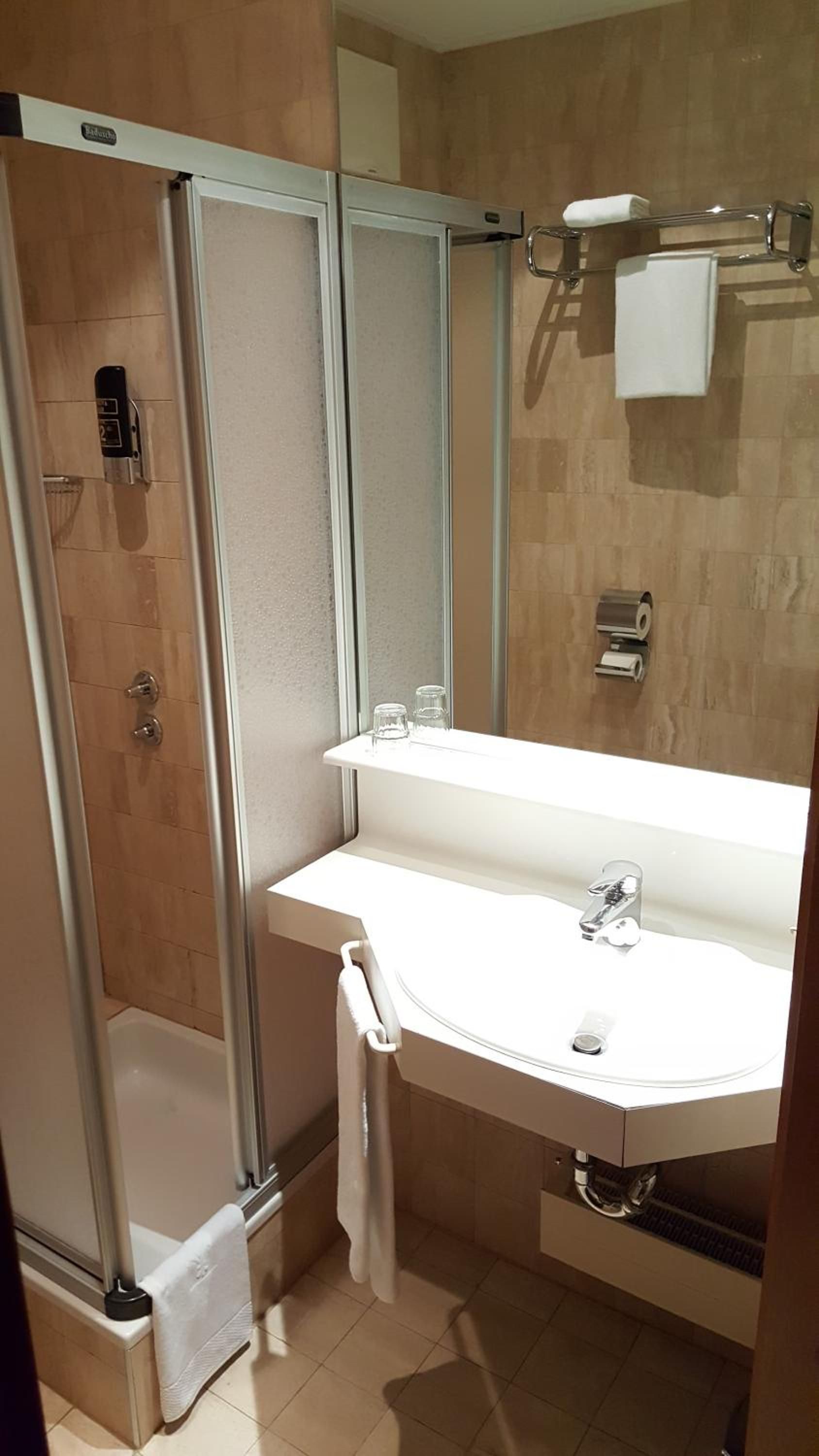 A modern bathroom with a glass-enclosed shower, a white sink with a mirror, and a towel rack.