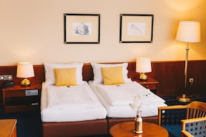 A hotel room with two beds, a nightstand with a lamp, a chair, and a table with a vase of flowers. - Paul S Hotel (Knittelfeld)