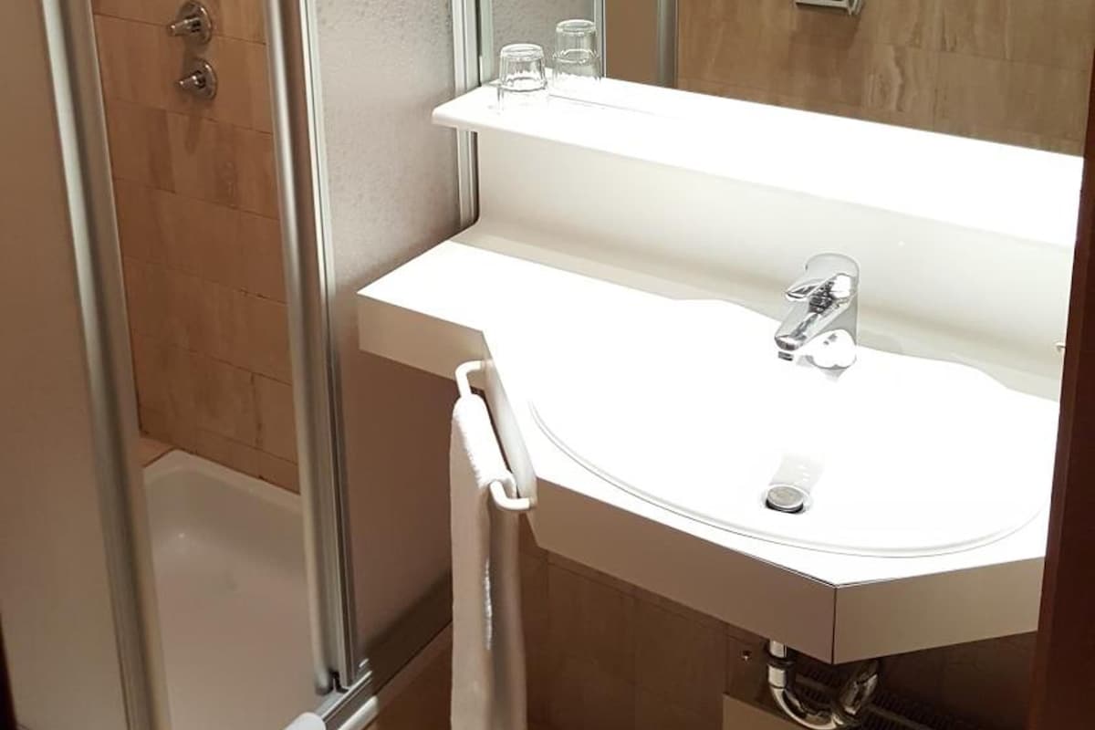 A modern bathroom with a glass-enclosed shower, a white sink with a mirror, and a towel rack.