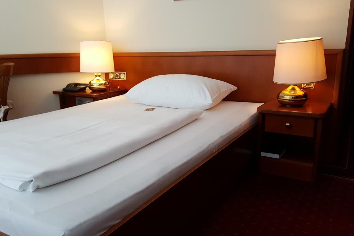 A hotel room with a single bed, two bedside lamps, a chair, and a nightstand with a telephone.