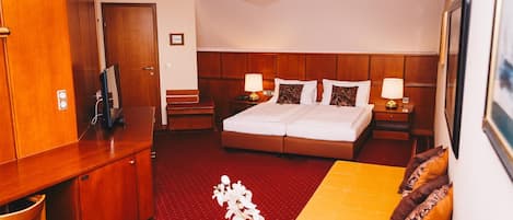 Habitación de hotel con cama, escritorio, silla, sofá, mesita, jarrón con flores y candelabro.