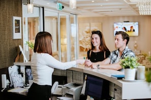 A reception desk with a receptionist, a guest, and a television screen in the background.