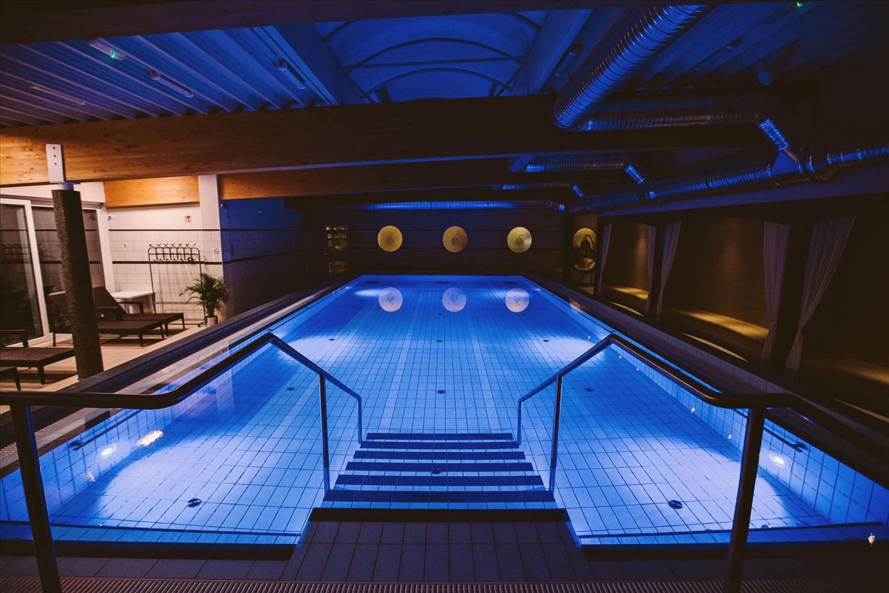 An indoor swimming pool with a tiled floor, a central staircase, and a ceiling with exposed beams and lighting fixtures.