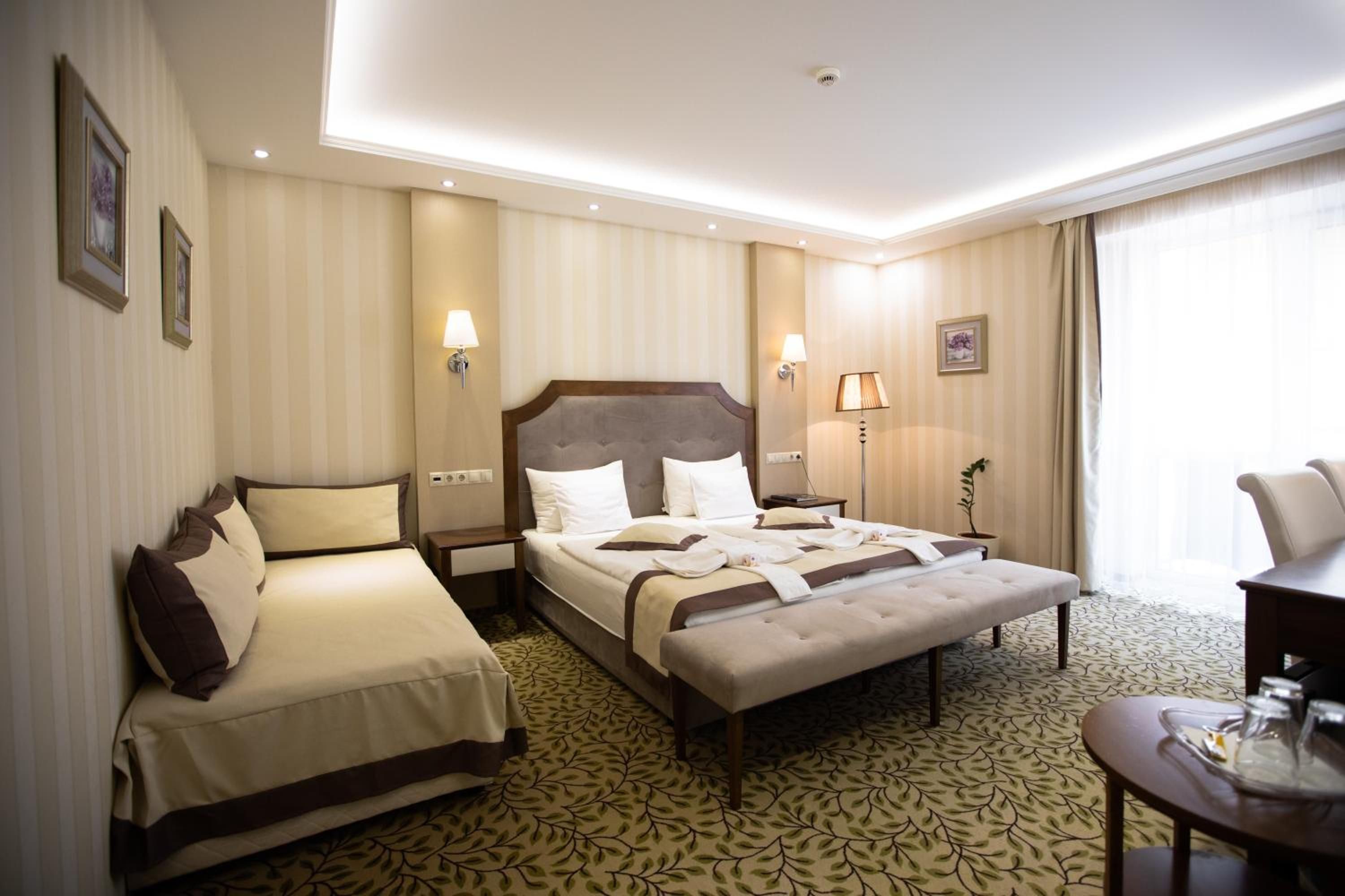 A hotel room with a double bed, a single bed, a desk, and a chair.