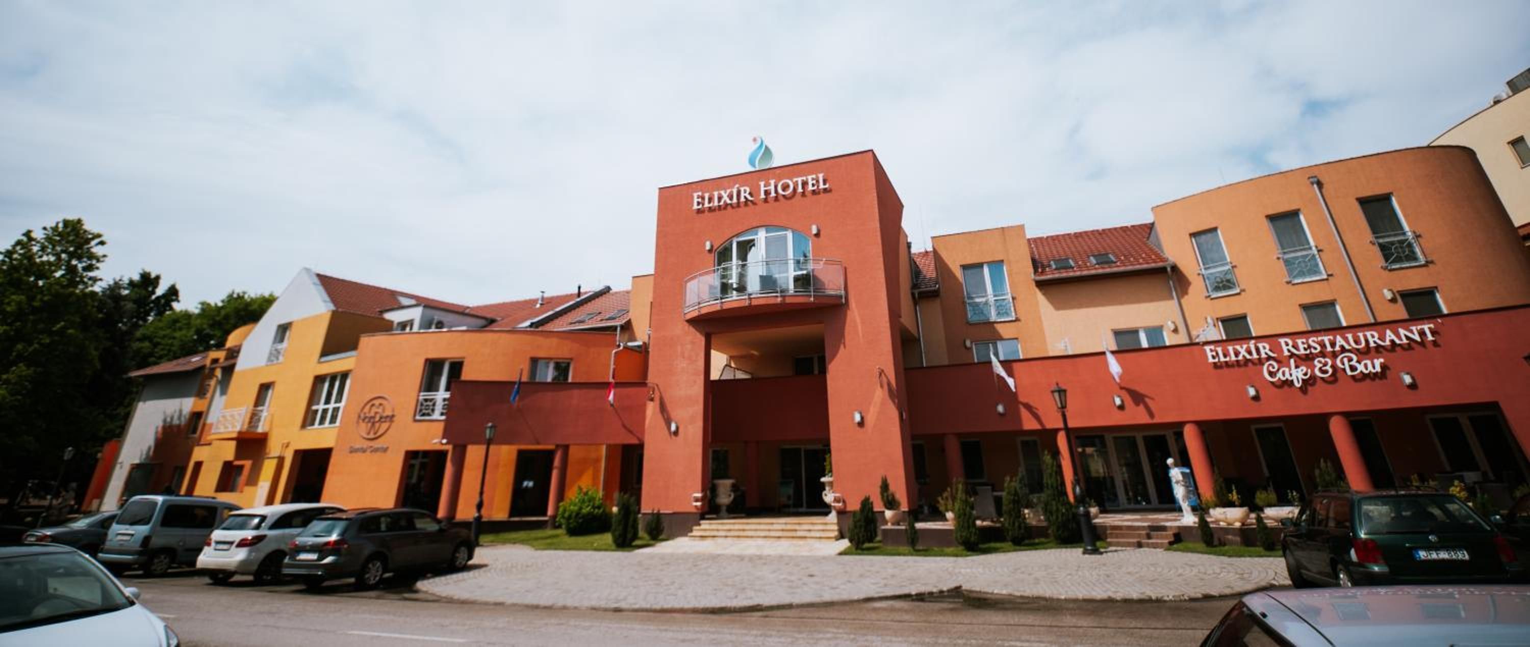 A hotel with a prominent red facade, a balcony, and a restaurant named 'Elixir Restaurant Cafe & Bar' at the ground level.