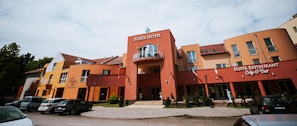 A hotel with a prominent red facade, a balcony, and a restaurant named 'Elixir Restaurant Cafe & Bar' at the ground level.