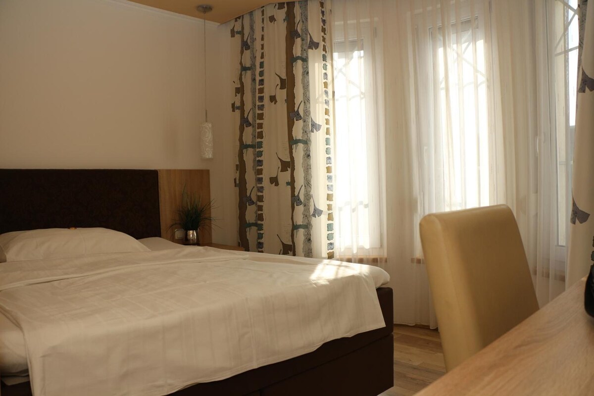 Una habitación de hotel con una cama, una silla y un ventanal con cortinas.