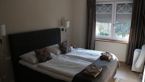 Ein Doppelbett mit weißen Leinentüchern, zwei Kissen, einer Nachttischlampe, einem Fenster mit Jalousien und einem Heizgerät.
