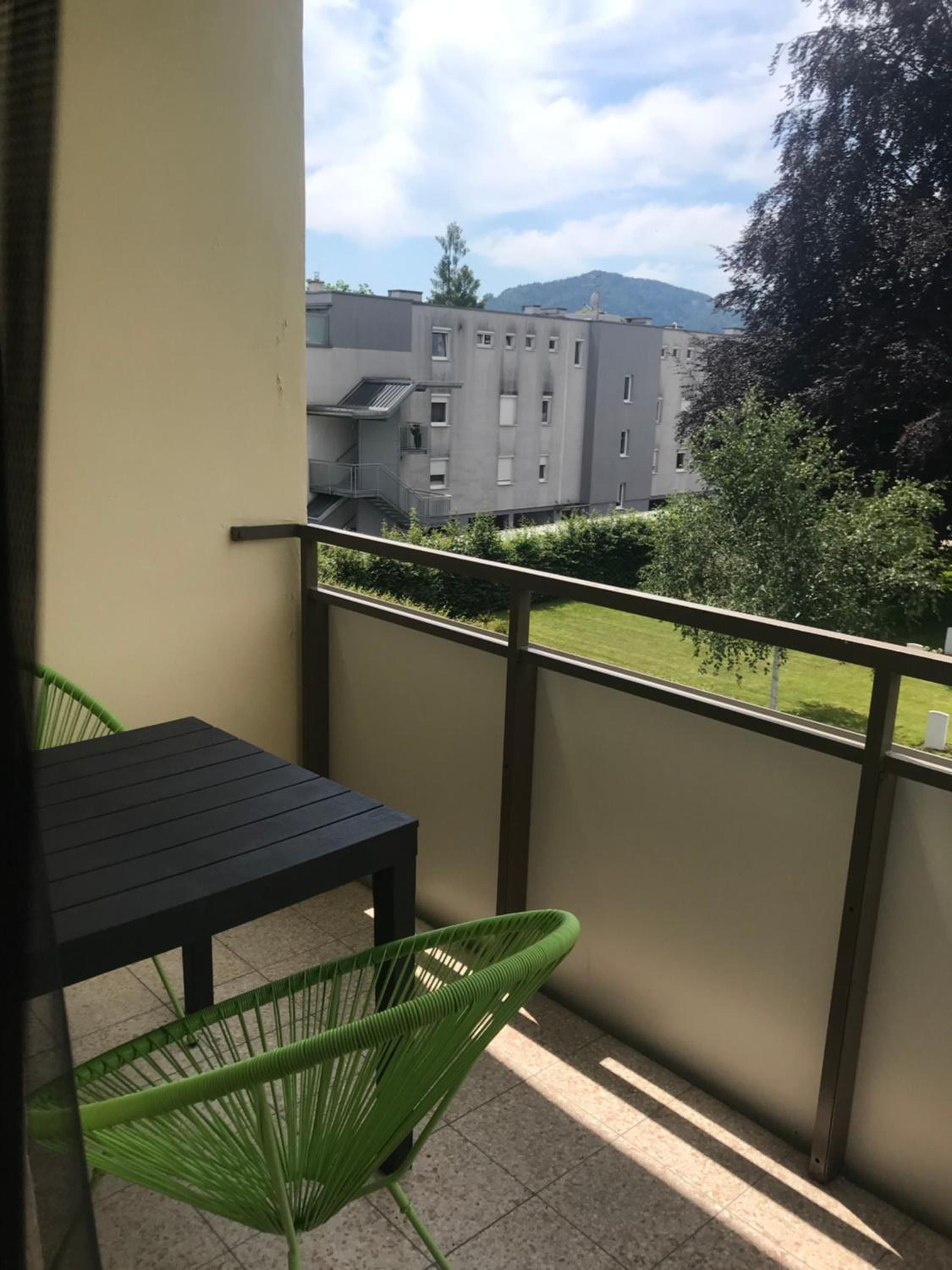 Ein Balkon mit Tisch und Stühlen mit Blick auf ein Gebäude und eine Rasenfläche.