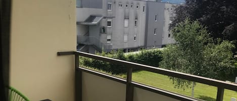 Un balcón con mesa y sillas, con vista a un edificio y una zona ajardinada.