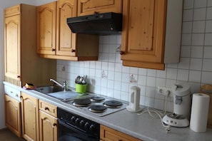 Una cocina con armarios de madera, un lavamanos de acero inoxidable, una estufa con cuatro hornallas y una cafetera.