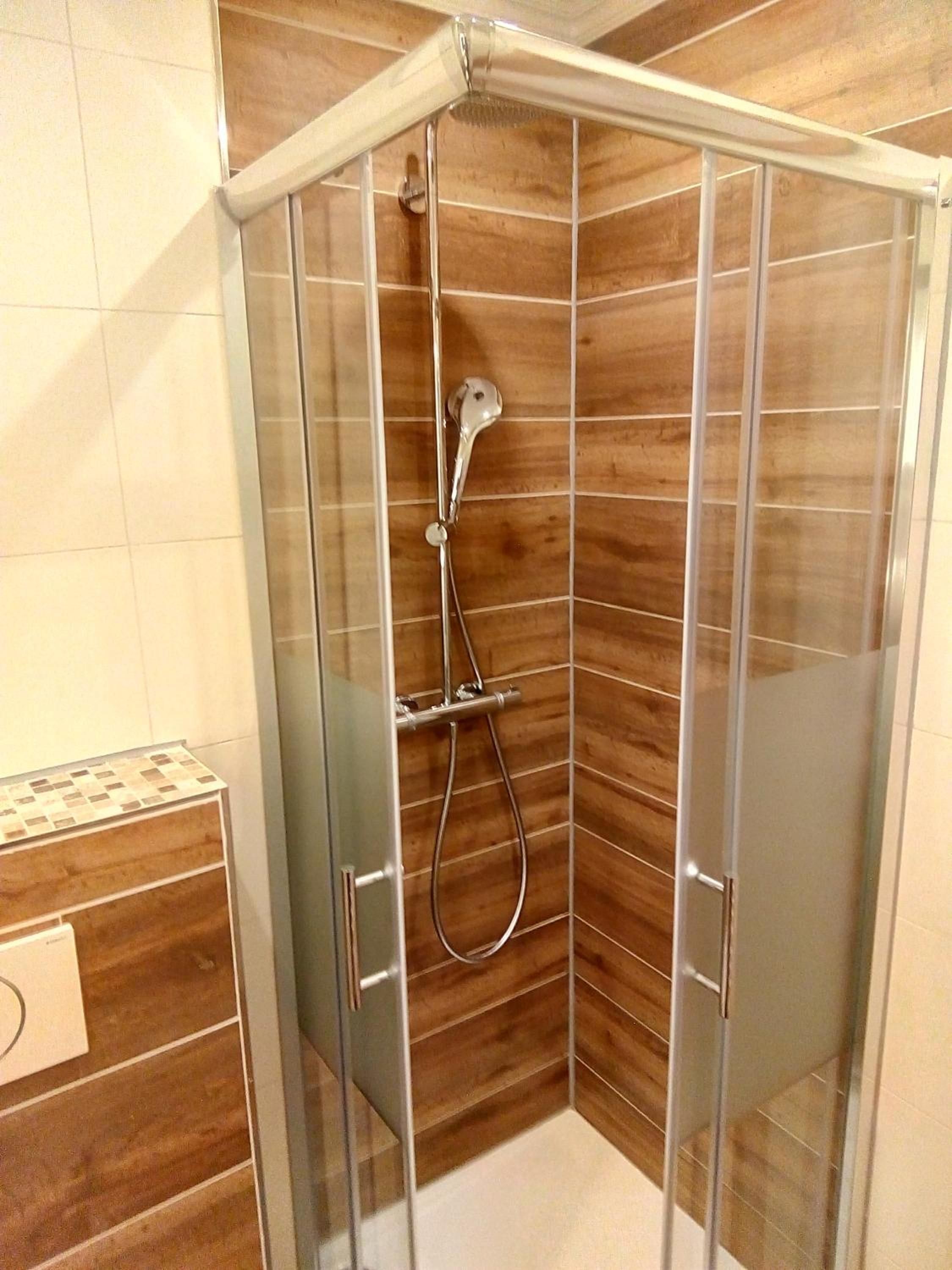 Eine gläserne Duschkabine mit Wandverkleidung aus Holz.