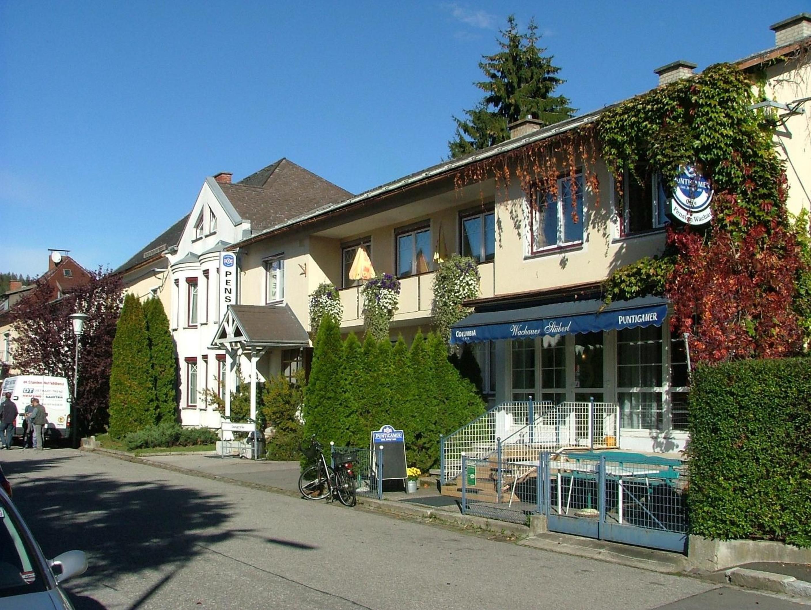 Straßenansicht mit einem Gebäude, auf dem 'PUNTIGAMER' steht, und einem Schild für 'Columbia Wachauer Stuben'.