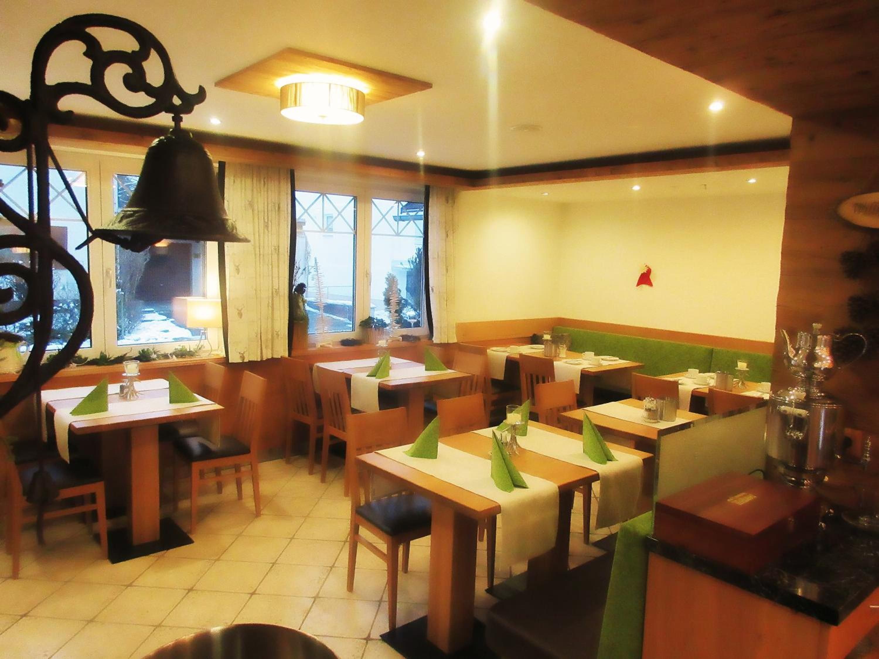 Ein Restaurant mit mehreren Tischen, Stühlen, einer Glocke und Blick ins Freie.