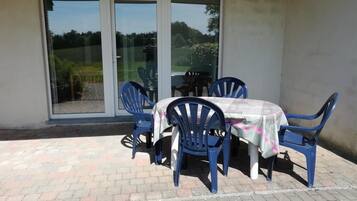 Un espace patio avec une table et des chaises, une porte-fenêtre coulissante et un sol en briques.