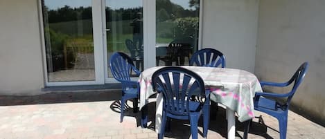 A patio area with a table and chairs, a sliding glass door, and a brick floor.