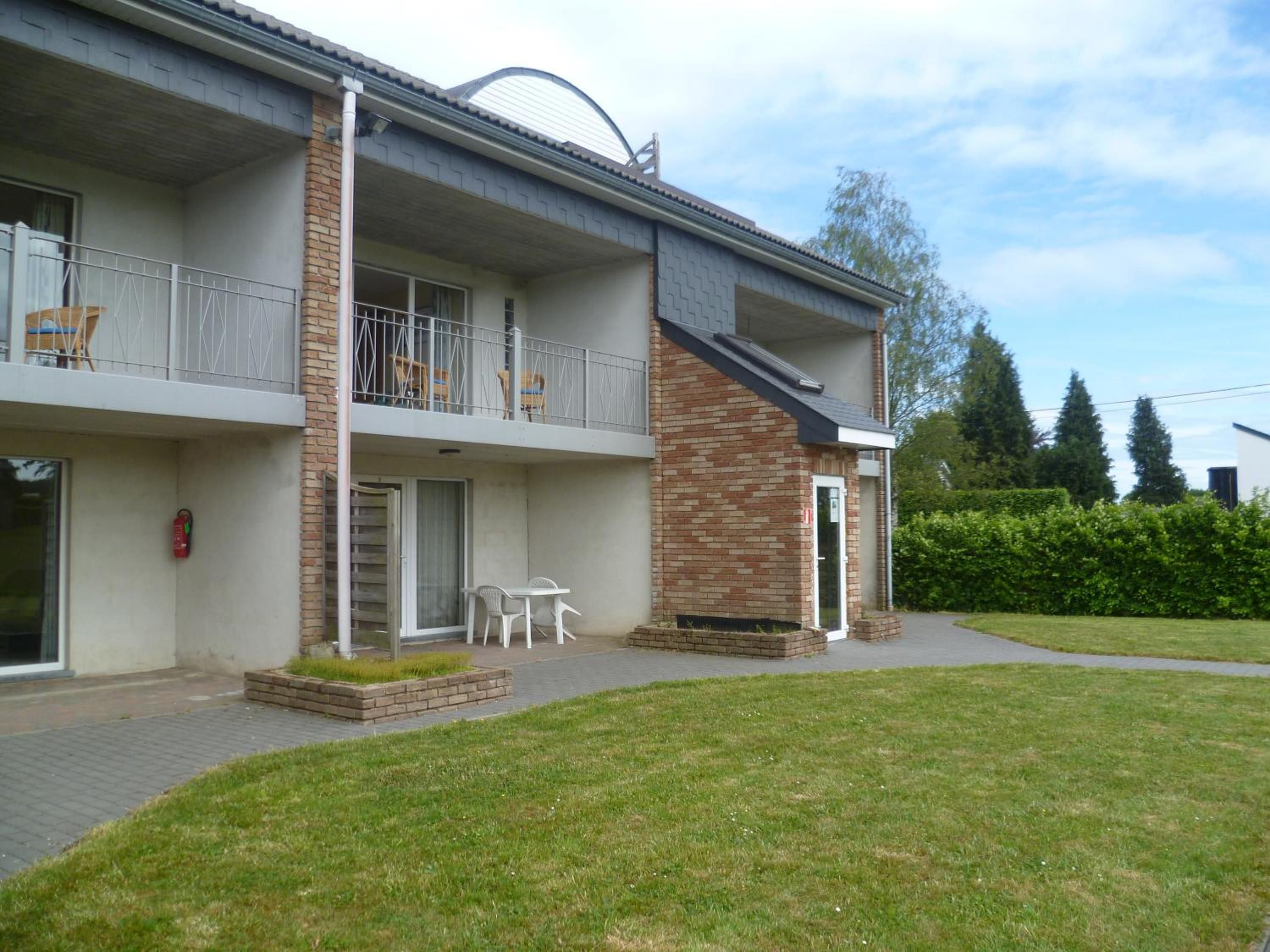 Un bâtiment à deux étages doté d’un balcon, d’un espace extérieur aménagé pour s’asseoir et d’une pelouse bien entretenue.