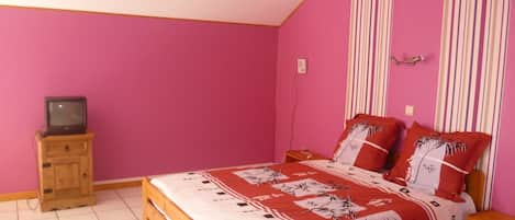 A bedroom with a bed, a wooden nightstand, a television on a cabinet, and a striped curtain.