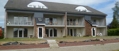 A two-story residential building with a flat roof, large windows, and a covered front porch.