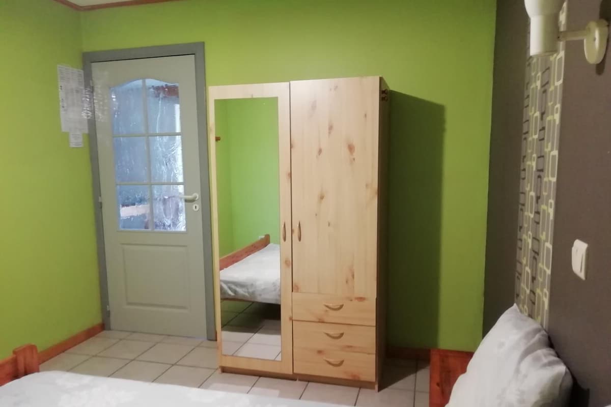 A bedroom with a bed, a wooden wardrobe with a mirror, a door with frosted glass, and a green wall.