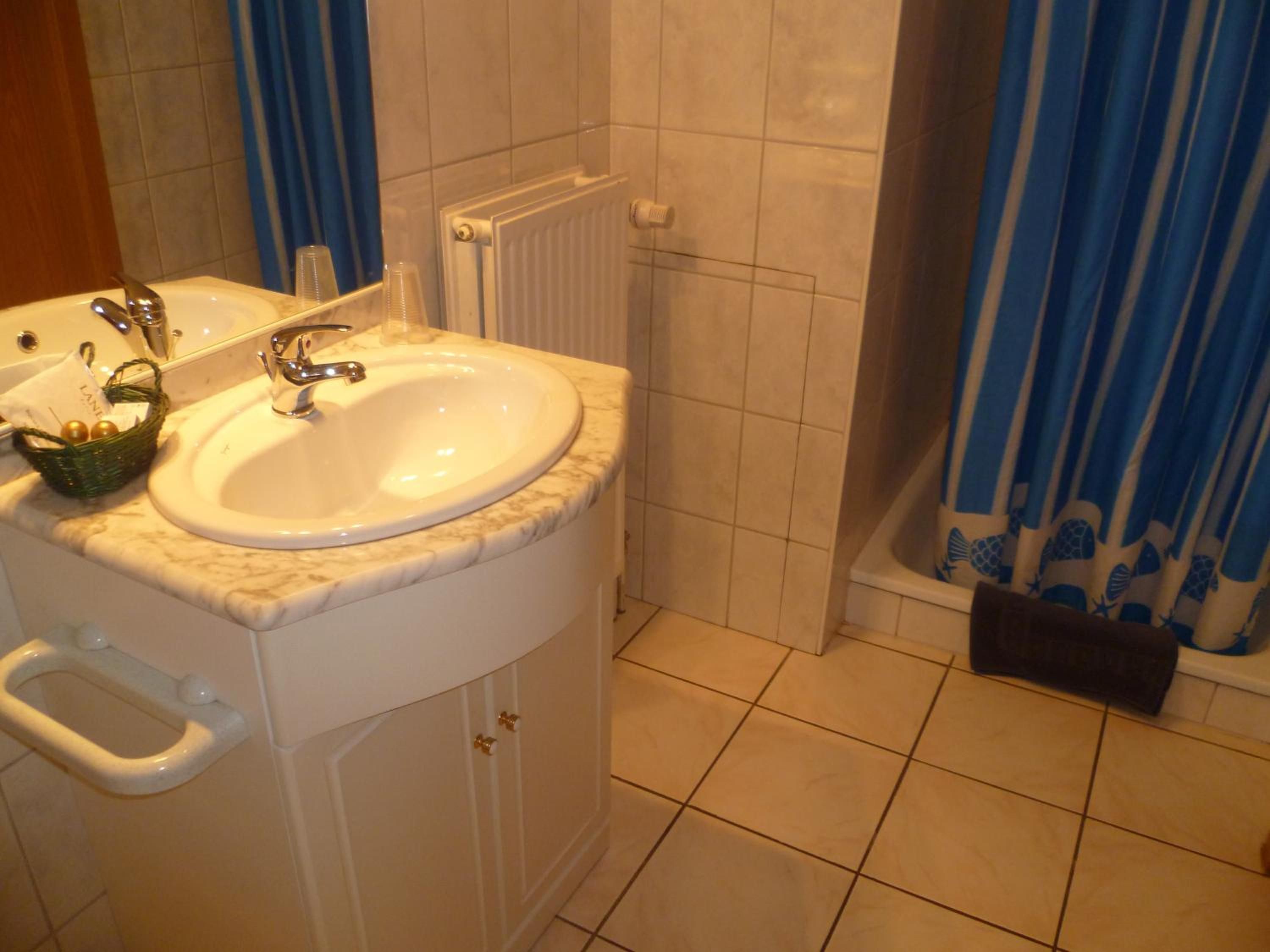 Une salle de bain avec un lavabo blanc, un miroir, un porte-serviettes et un rideau de douche.