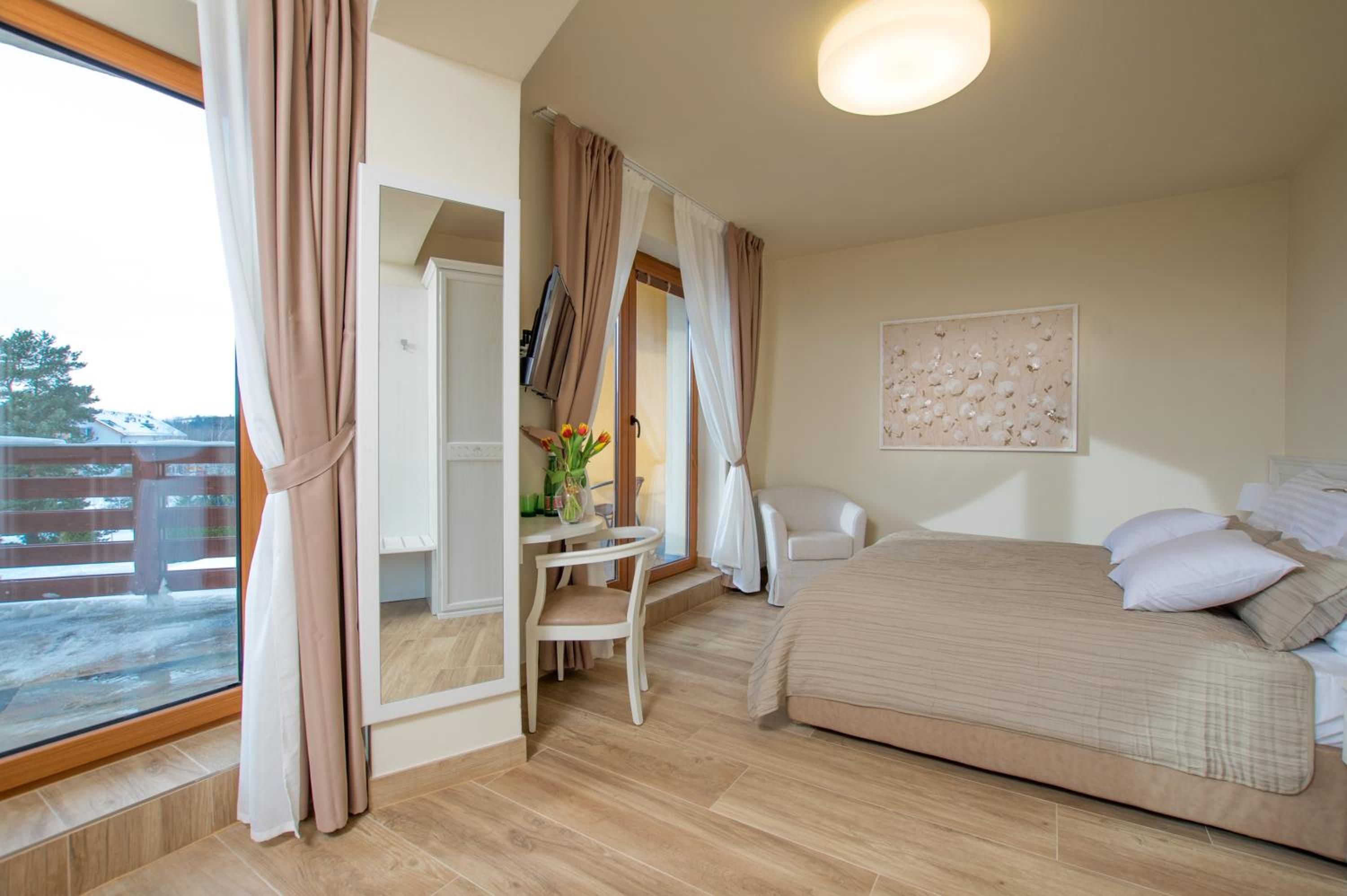 Ein Schlafzimmer mit einem Bett, einem Sessel, einem Tisch mit Blumen und einem Fenster mit Vorhängen.
