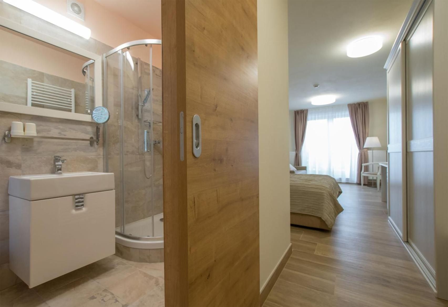A hotel room with a bathroom, a shower, a bed, and a bedside table.