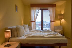 Quarto de hotel com cama, abajures, janela com cortinas e vista para a cidade.