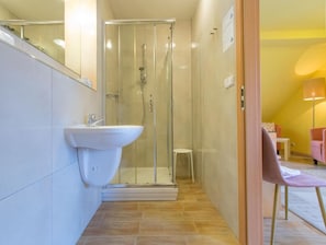 Uma casa de banho moderna com cabine de duche de vidro, lavatório branco e um pequeno banquinho.