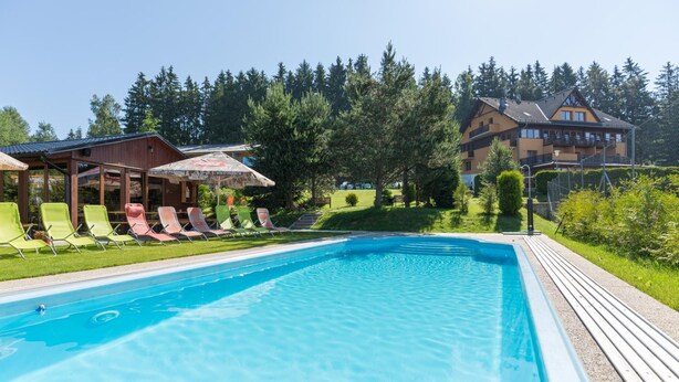 A swimming pool with lounge chairs and a wooden deck. - Hotel Slune Anva Louka (Lipno nad Vltavou)